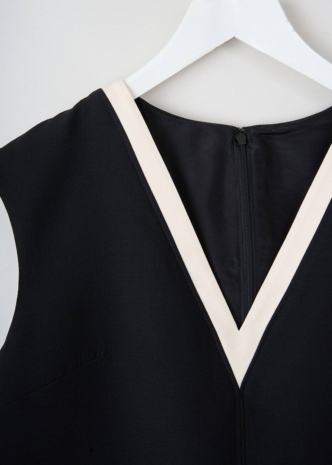 Close-up of black sleeveless midi dress by Valentino, highlighting the white trim on the V-neckline and concealed back zip. Available at a discounted price at Kiki's Stocksale in Maastricht.